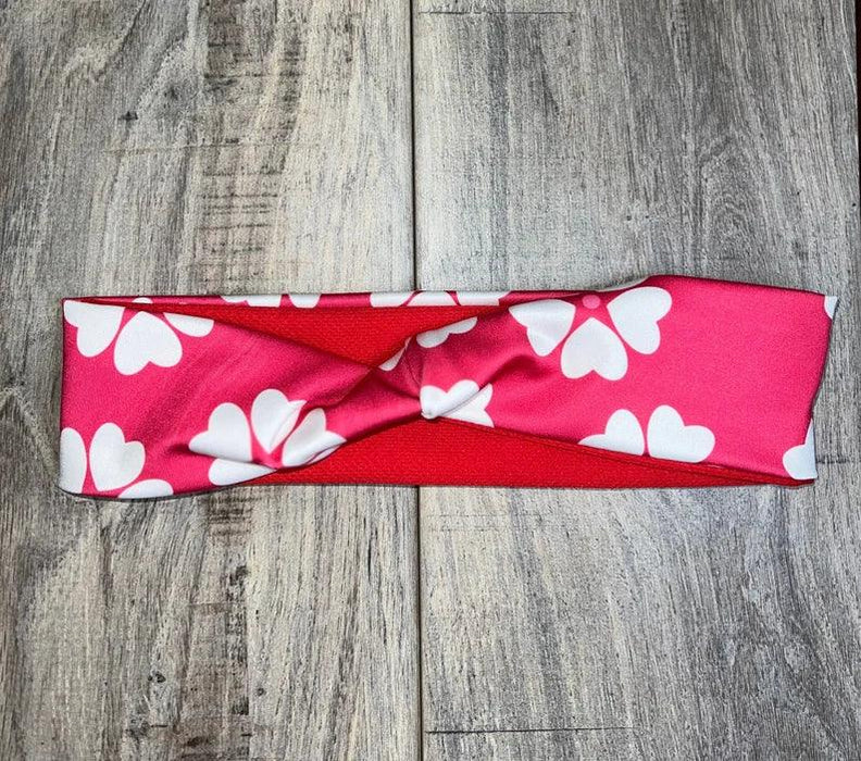 Pink workout headband with white flower pattern, laid flat on wood background, Athena Fitness Collections
