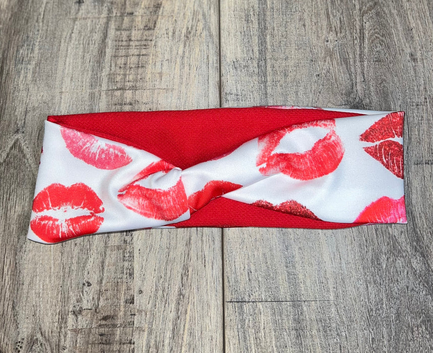 Red and white workout headband with red lip print pattern, handmade and twisted style on wood surface