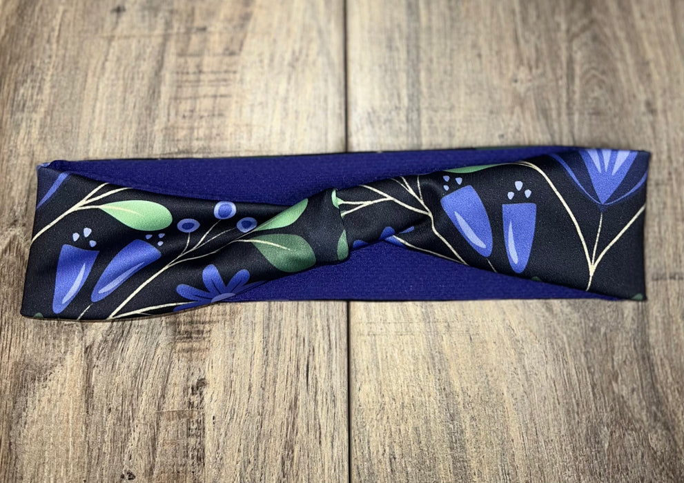 Handmade workout headband with blue floral pattern and green leaves on navy background, laid on wooden surface