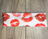 Handmade white workout headband with red lipstick kiss prints, displayed on wooden surface