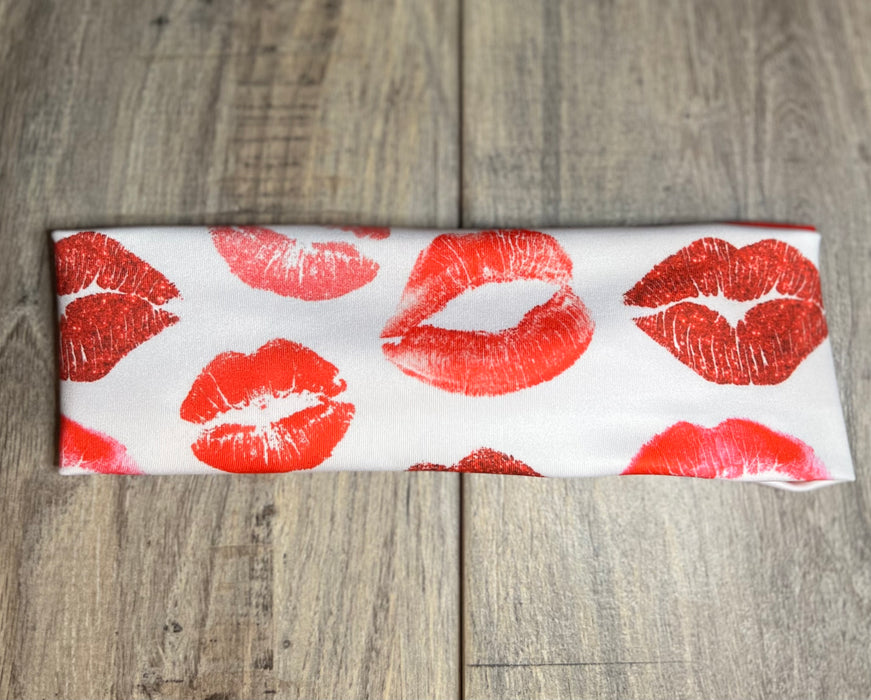 Handmade white workout headband with red lipstick kiss prints, displayed on wooden surface