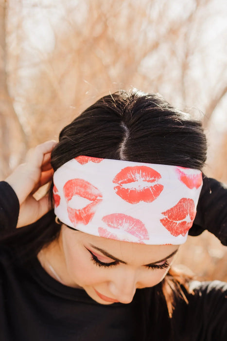 Woman outdoors wearing black workout top, maroon leggings, and white headband with red lip prints