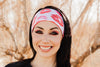 Smiling woman wearing black workout top and white headband with red kiss prints outdoors