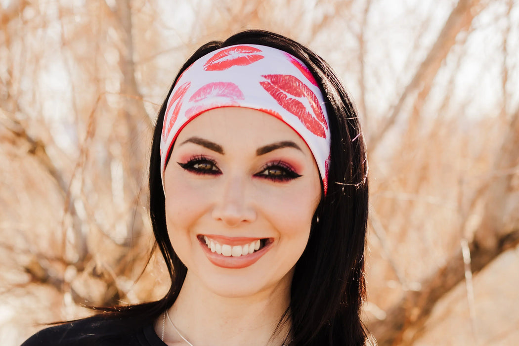 Smiling woman wearing black workout top and white headband with red kiss prints outdoors