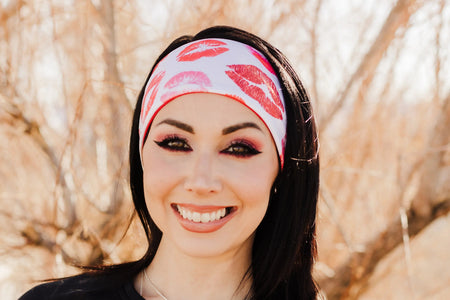 Smiling woman wearing black workout top and white headband with red kiss prints outdoors