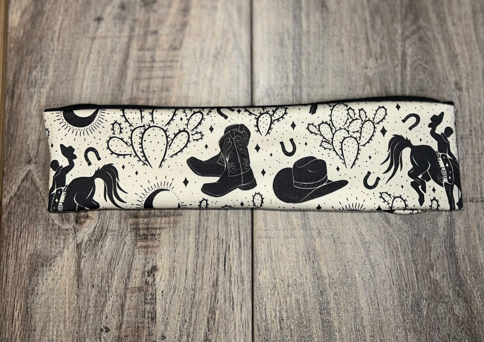 Handmade workout headband with black western cowboy design including boots, hat, horse, cactus, and horseshoes on cream fabric