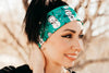 Woman smiling outdoors wearing a teal workout headband with snowman prints and a black shirt