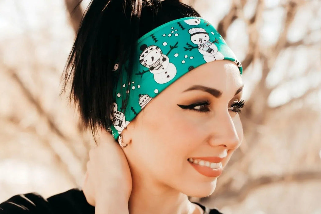 Woman smiling outdoors wearing a teal workout headband with snowman prints and a black shirt