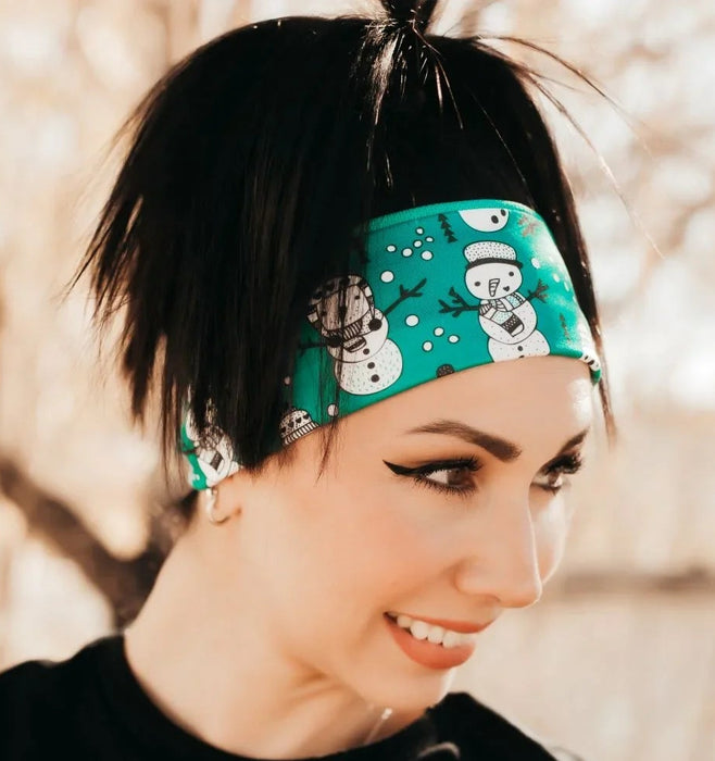 Woman wearing a teal workout headband with white snowman prints and a black top outdoors