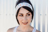 Woman wearing a floral workout headband and white tank top, posing outdoors with a soft smile