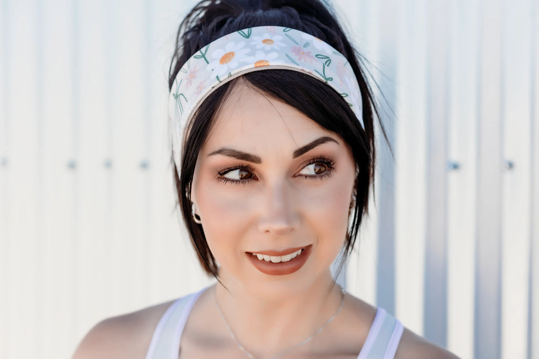 Woman wearing a floral workout headband and white tank top, posing outdoors with a soft smile