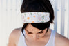 Woman wearing white floral workout headband with daisies, looking down, in athletic tank top