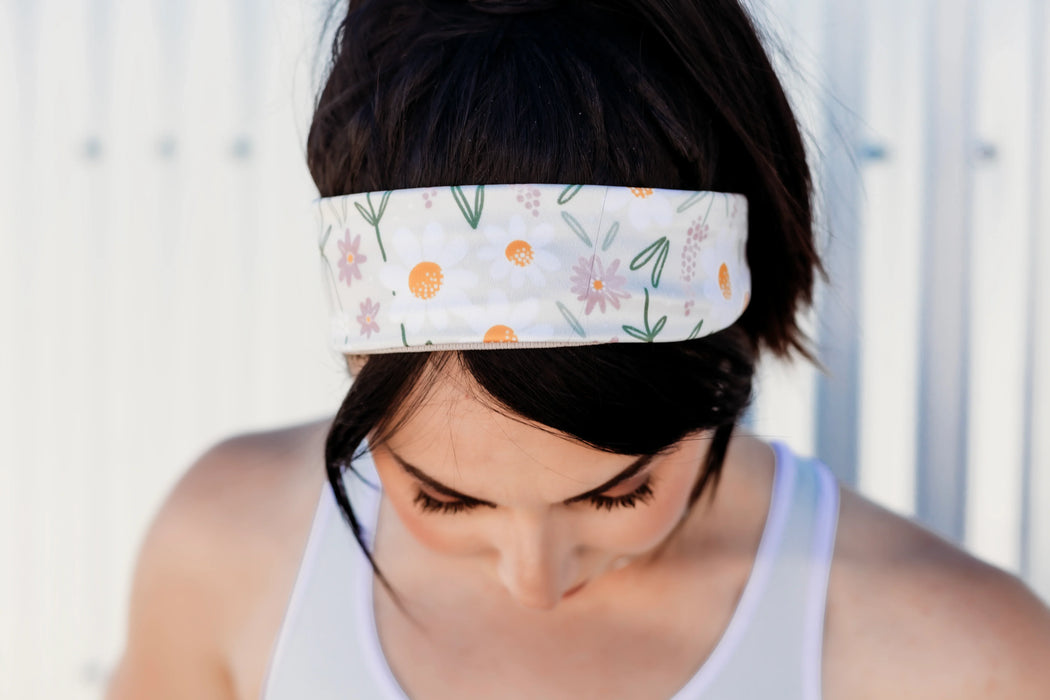 Woman wearing white floral workout headband with daisies, looking down, in athletic tank top