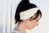 Woman smiling wearing white sunflower print workout headband with ponytail against light background