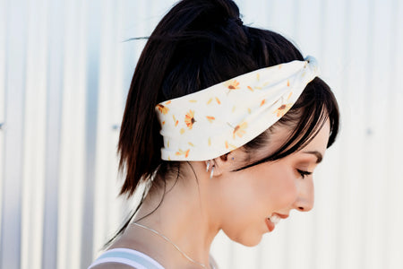 Woman smiling wearing white sunflower print workout headband with ponytail against light background