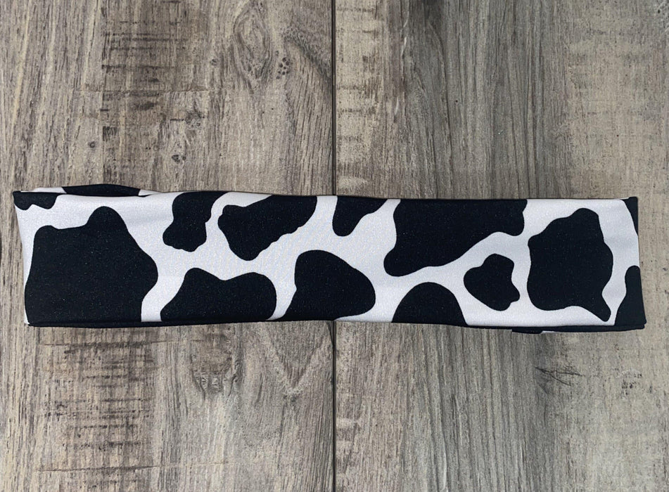 Black and white cow print workout headband laid flat on wood surface from Athena Fitness Collections