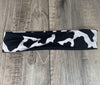 Black and white cow print workout headband lying flat on wooden surface, handmade gym accessory