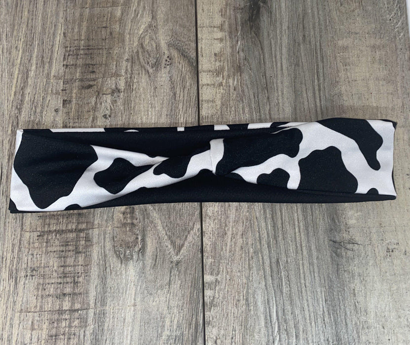 Black and white cow print workout headband lying flat on wooden surface, handmade gym accessory