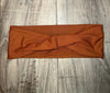 Rust-colored ribbed fabric workout headband with twist knot detail on wood floor