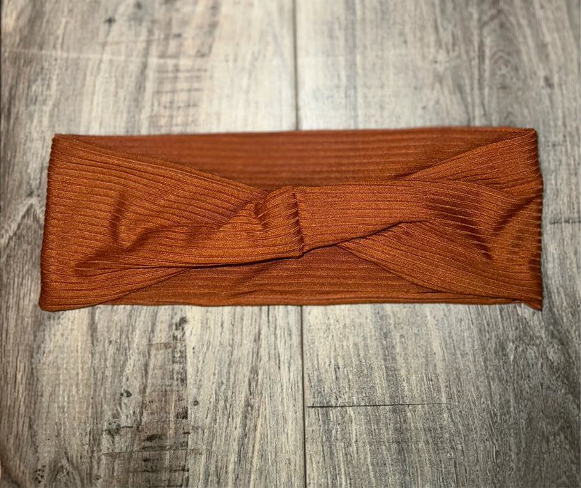 Rust-colored ribbed fabric workout headband with twist knot detail on wood floor