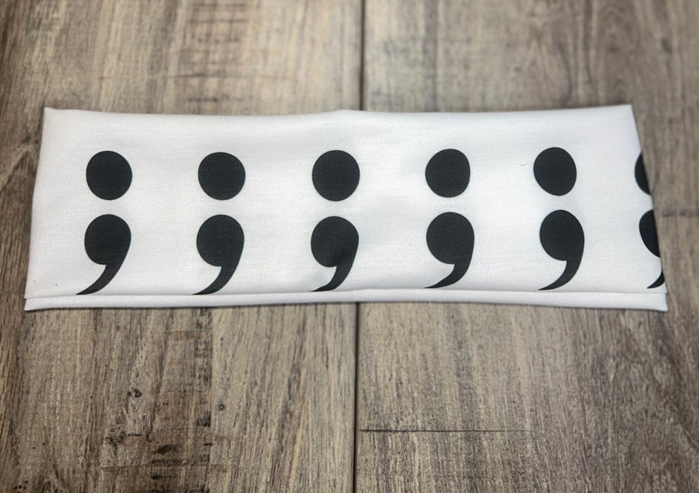 White workout headband with repeated black semicolon design on wooden surface, Athena Fitness Collections