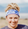 Smiling woman wearing blue patterned workout headband and purple t-shirt outdoors in natural setting