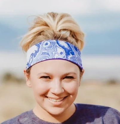 Smiling woman wearing blue patterned workout headband and purple t-shirt outdoors in natural setting