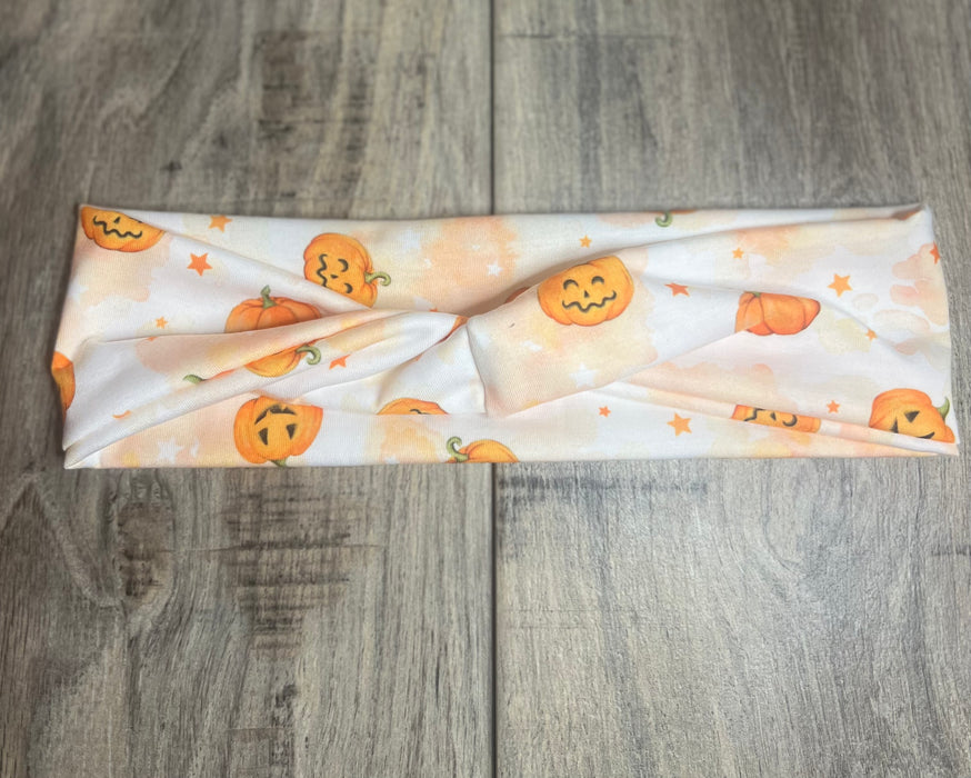 White twisted workout headband with orange Halloween pumpkin and star print on wooden surface