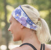 Blonde woman wearing a floral purple workout headband and black strappy fitness top outdoors