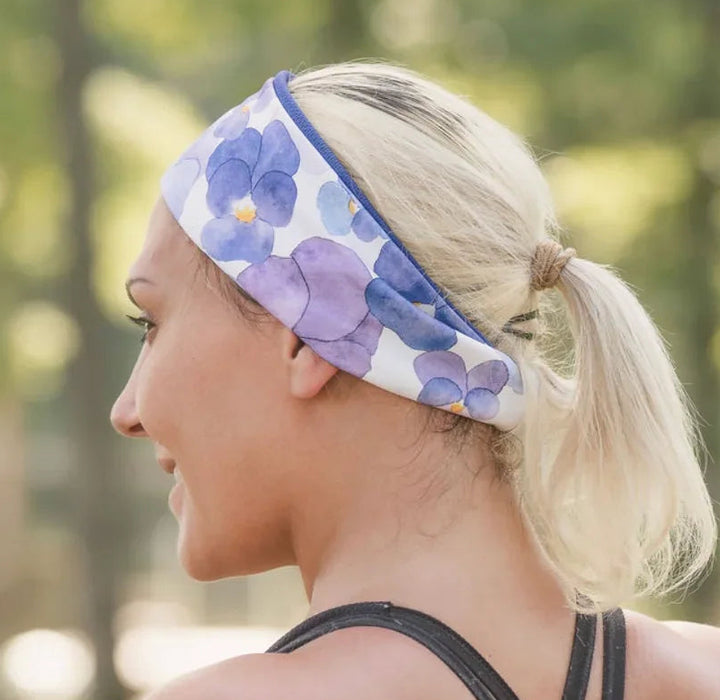 Blonde woman wearing a floral purple workout headband and black strappy fitness top outdoors
