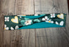 Handmade workout headband with green fabric featuring white flowers and yellow hearts, laid on wooden surface