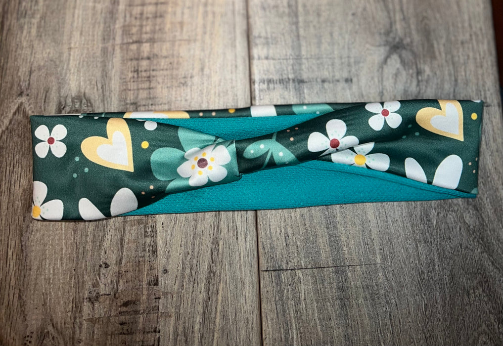 Handmade workout headband with green fabric featuring white flowers and yellow hearts, laid on wooden surface