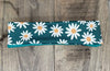 Handmade workout headband with white daisy flower pattern on teal background, laid on wooden surface