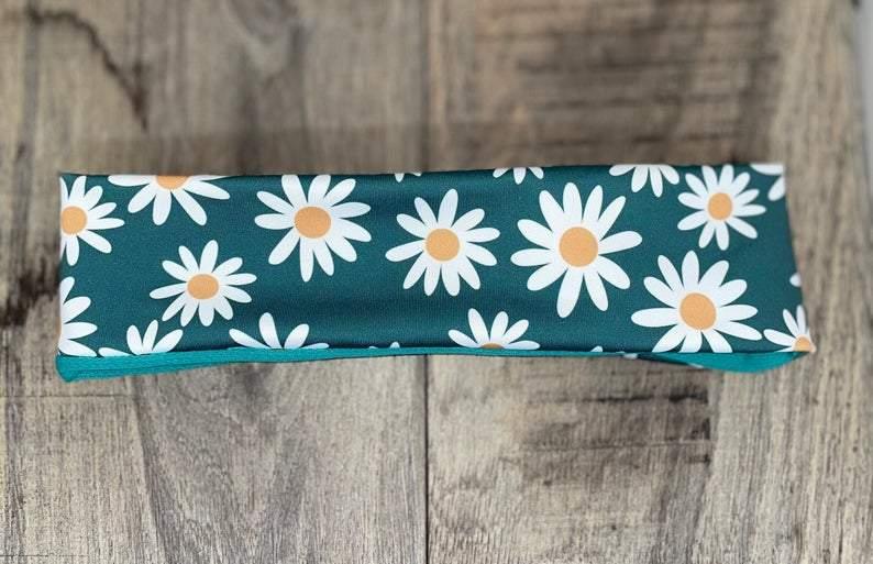 Handmade workout headband with white daisy flower pattern on teal background, laid on wooden surface