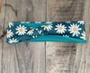 Handmade workout headband with white daisy pattern on teal fabric, laid on wooden surface