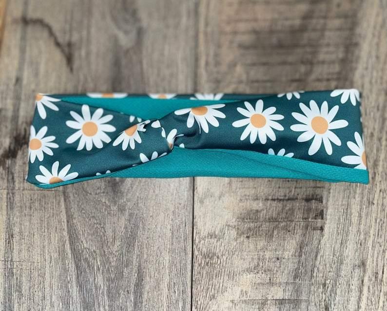 Handmade workout headband with white daisy pattern on teal fabric, laid on wooden surface