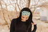Woman outdoors wearing a green and white floral workout headband from Athena Fitness Collections with bare trees background