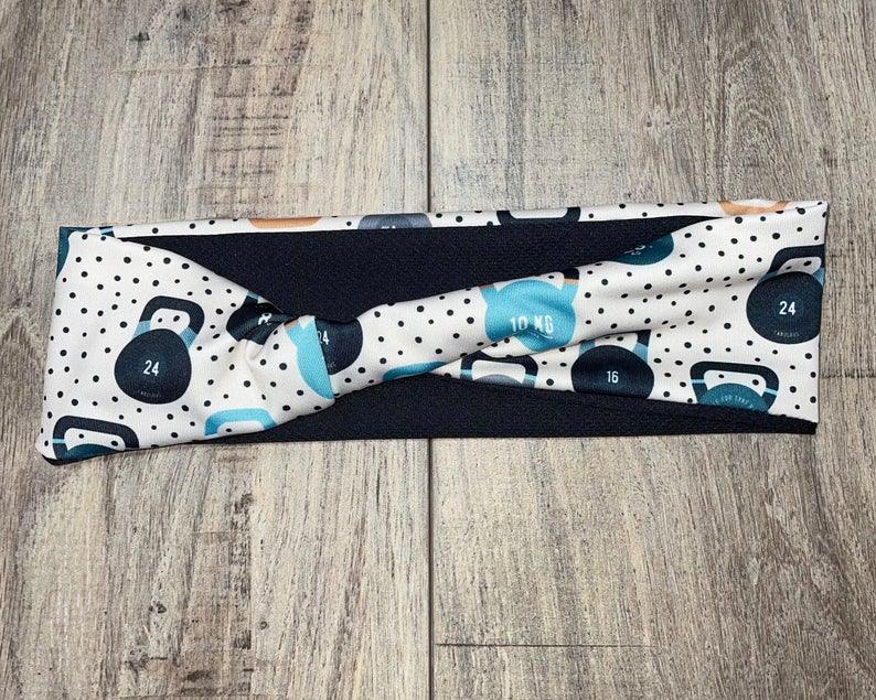 Close-up of a handmade fitness headband with a kettlebell print in black, blue, and white on a wooden floor